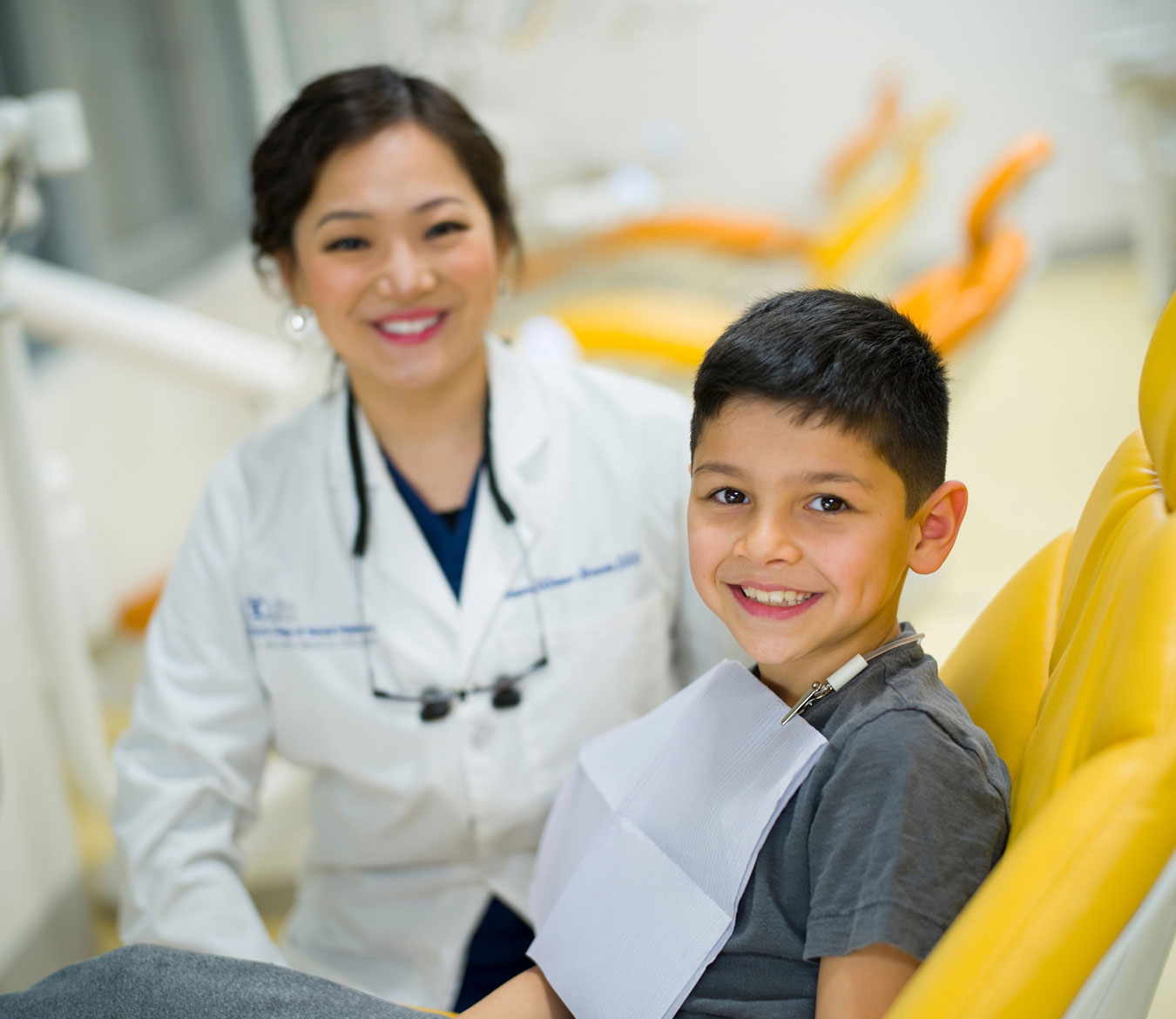 Dentist smiling next to young male patient in chair.