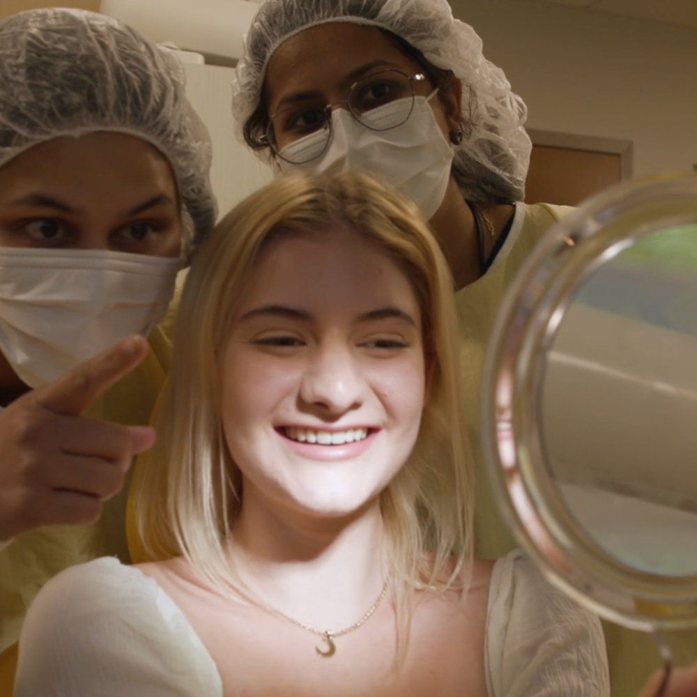 girl smiling in mirror after having braces removed